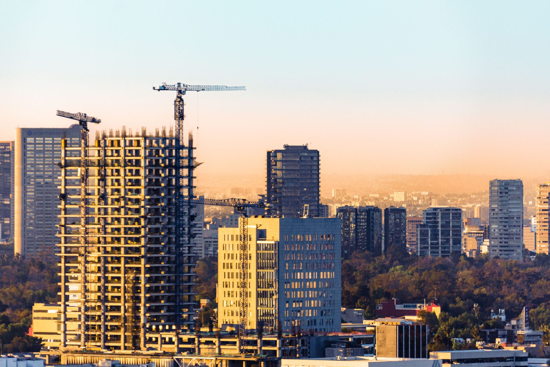 Aerial view of construction cranes and skyscrapers in Ciudad de México at sunset.